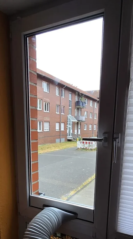 Abluftschlauch eines Klimageräts durch ein gekipptes Fenster in Köln