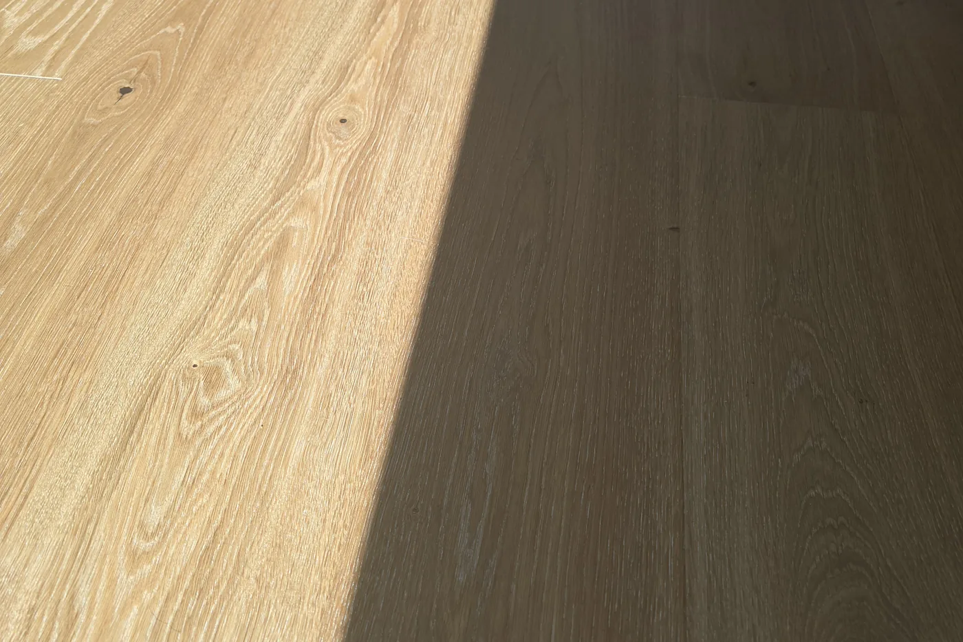 Direkte Sonne fällt über einen Eichenparkettboden, eine Hälfte hell beschienen, die andere im Schatten
