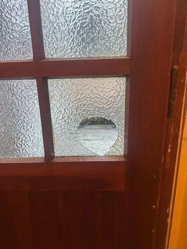 Kaputte Ornamentglasscheibe mit Loch in einer Holztür, vor dem Scheibentausch