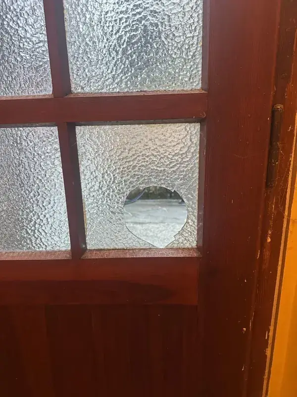 Kaputte Ornamentglasscheibe mit Loch in einer Holztür, vor dem Scheibentausch